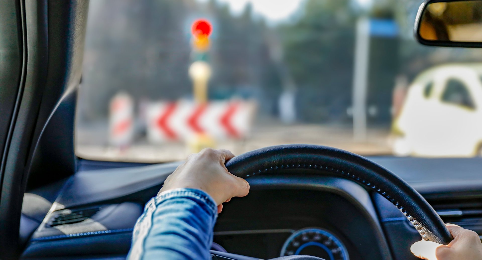 Hands holding a black steering wheel stopped at a traffic light, viewed through the windshield